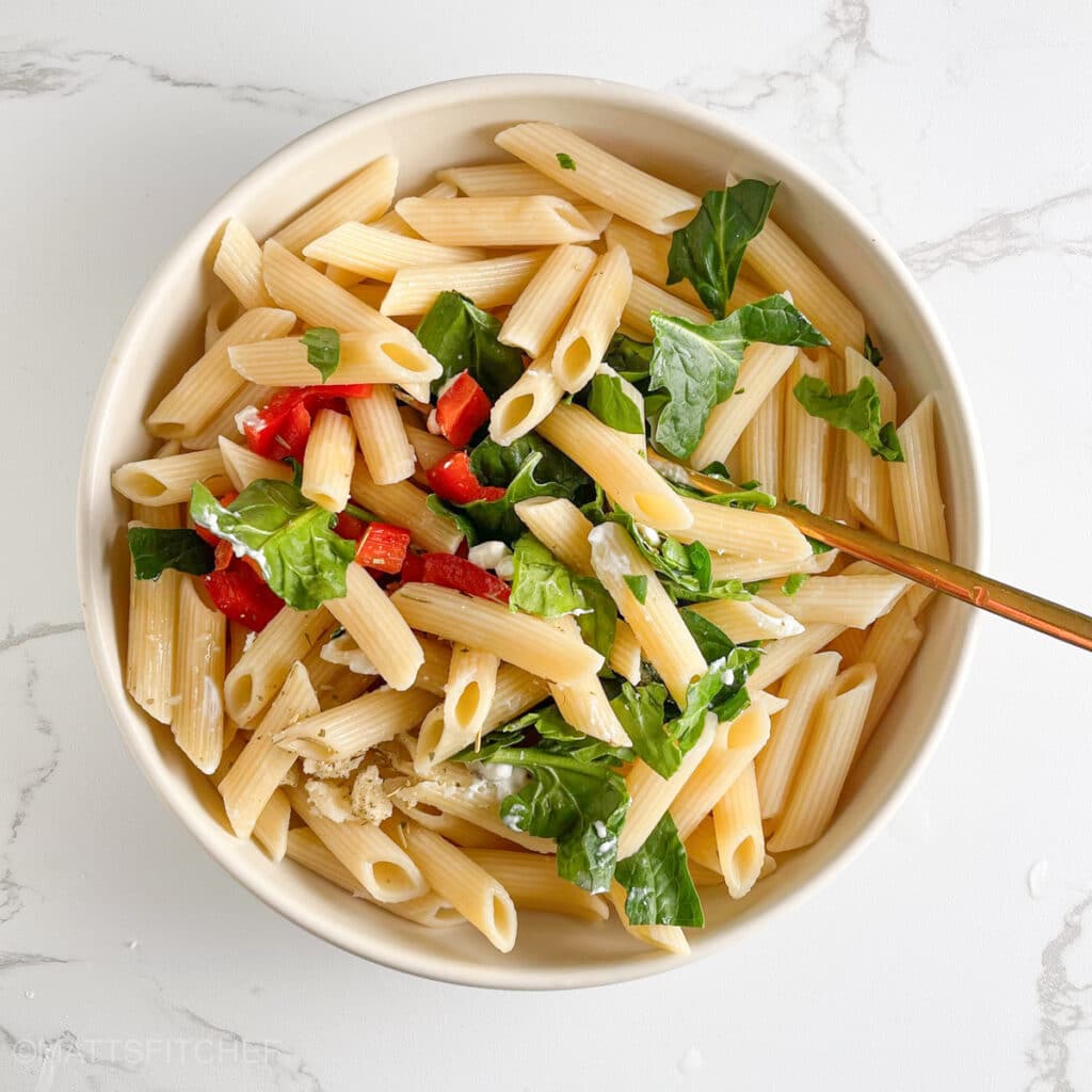 Mixing ingredients for a low calorie pasta salad with a golden fork.