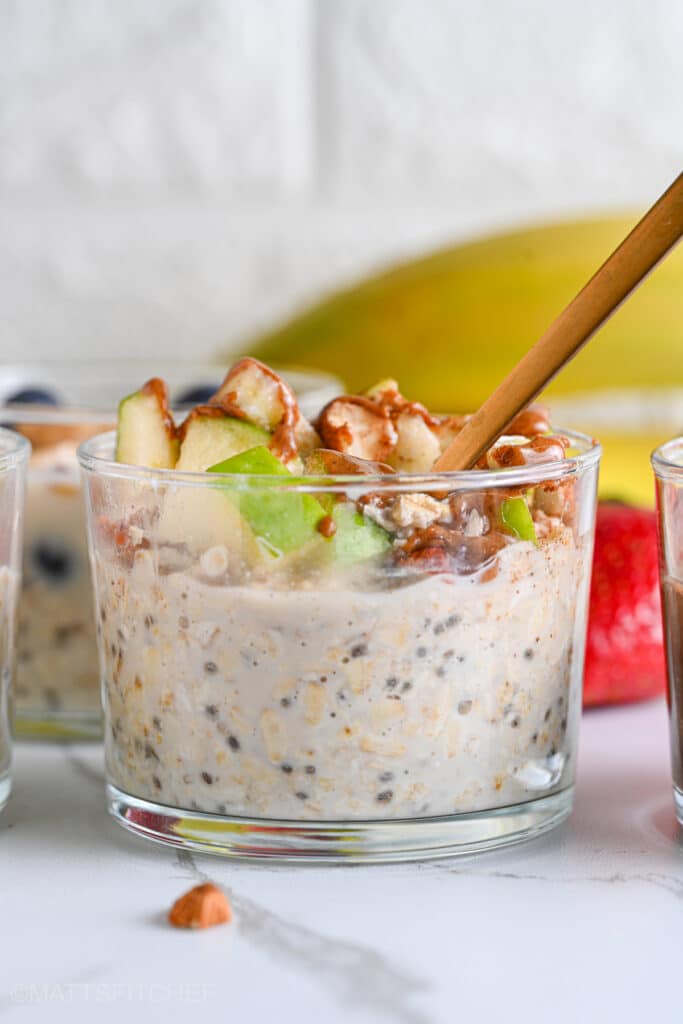 Low calorie overnight oats topped with apple and almond butter, being served with a golden spoon