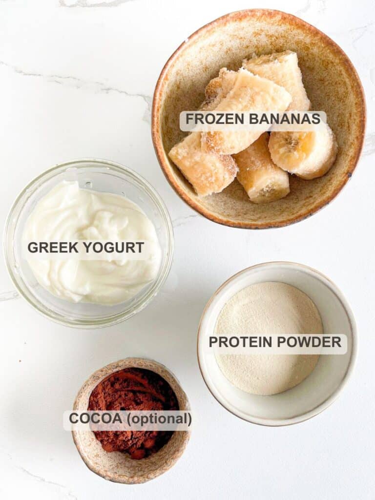 Protein Ice Cream Ingredients layer over a marble table &ndash; frozen bananas, plain Greek yogurt, protein powder and optionally cocoa powder.