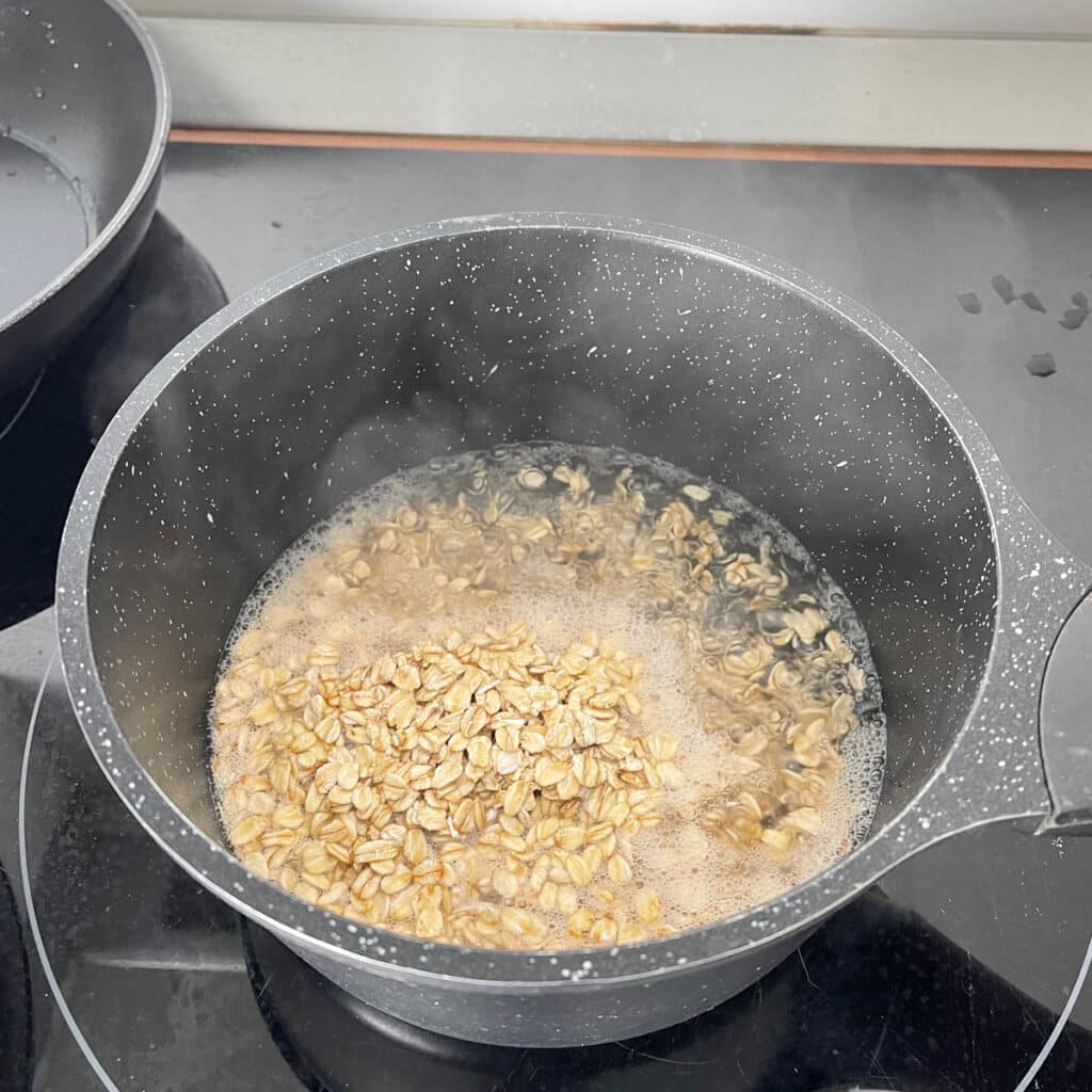 Rolled oats added to a pot of boiling water, ready to simmer for a savory porridge