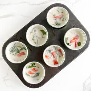 Blended egg whites and cottage cheese mixture divided in lined muffin tins, ready for baking in the oven