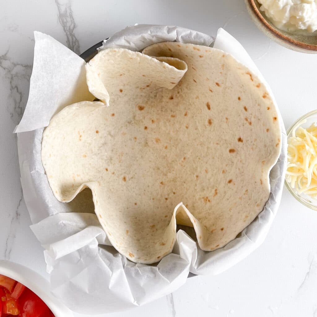 Tortilla wrap placed in a round baking pan, ready to be filled with egg mixture.