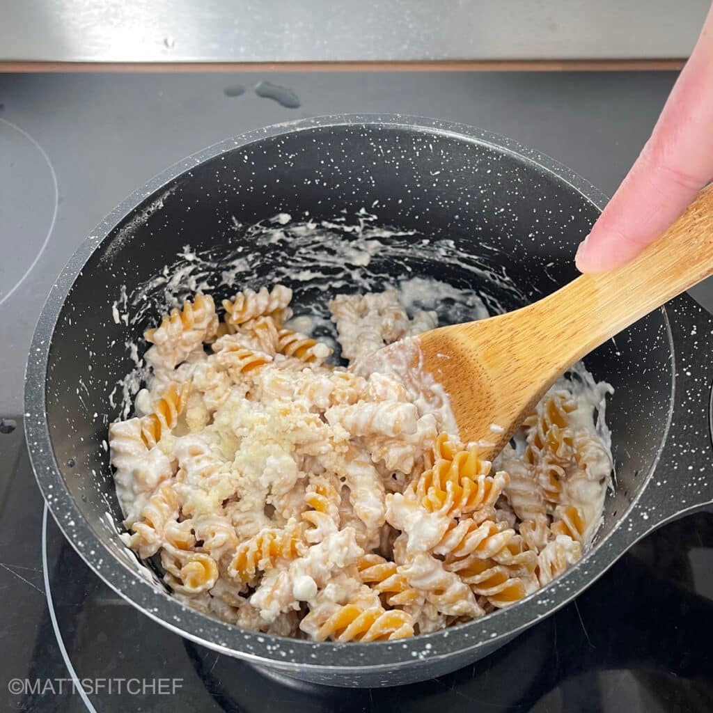 Stirring protein pasta sauce with Parmesan cheese for a creamy pasta dish