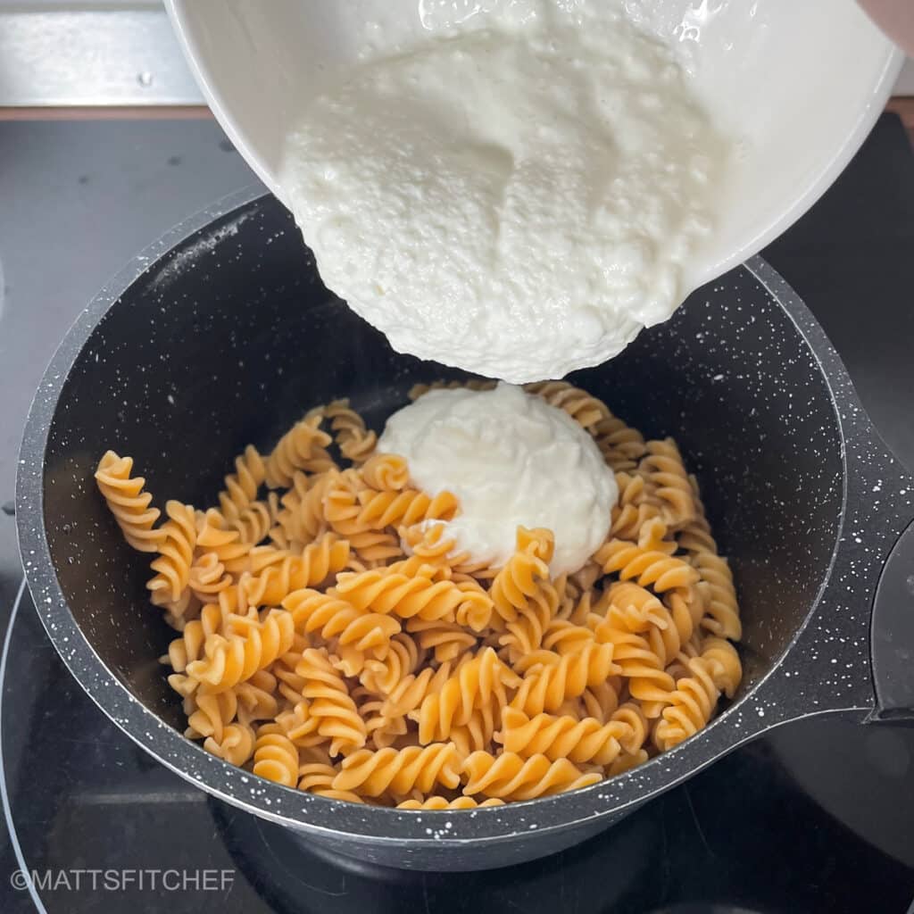 Pouring cottage cheese pasta sauce to cooked rotini