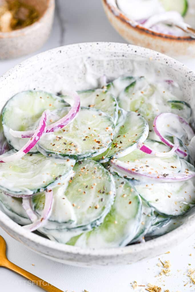 Front view of high protein cucumber yogurt salad topped with freshly cracked black pepper and sliced onion