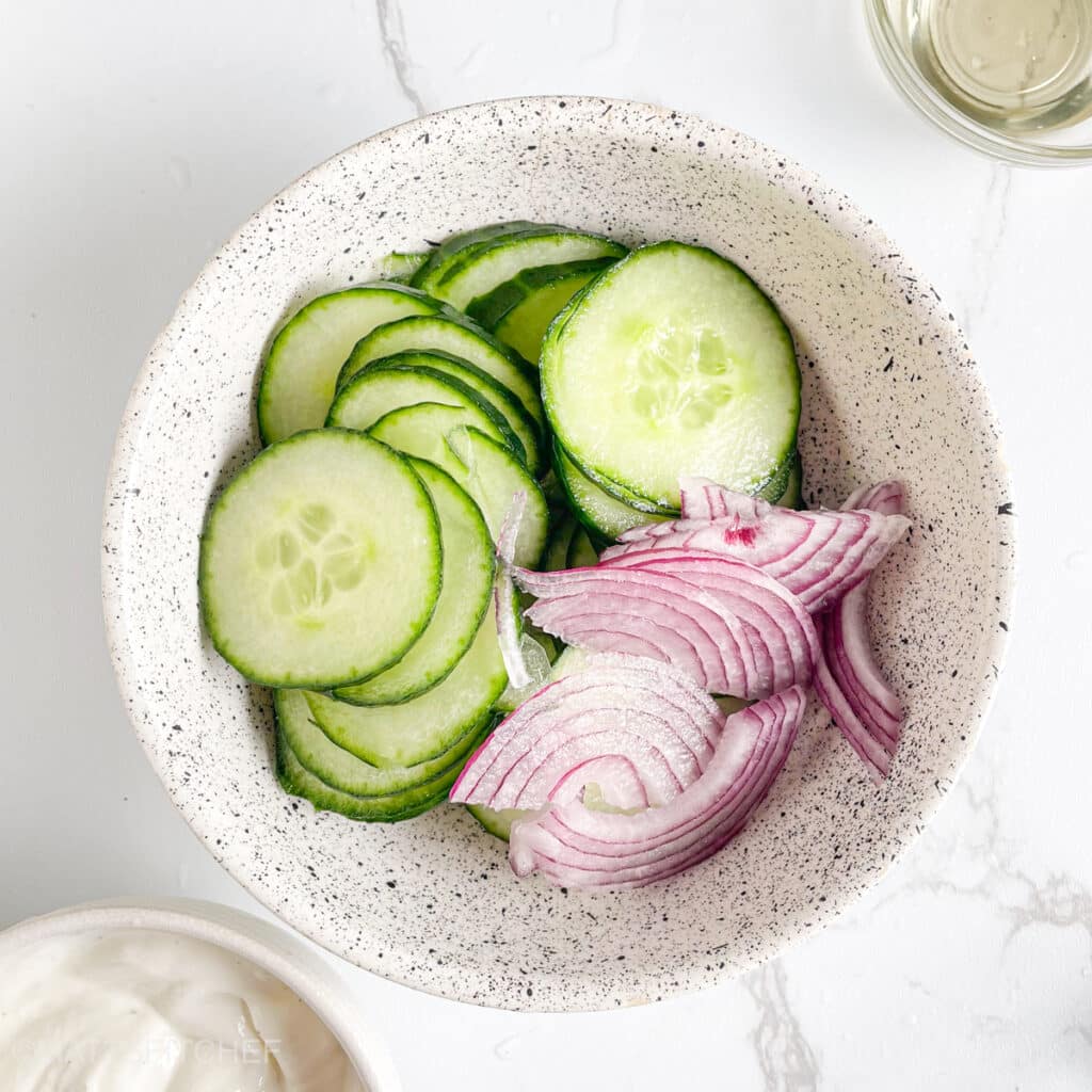 Sliced cucumber and sliced onion in a bowl, ready to add Greek yogurt dressing