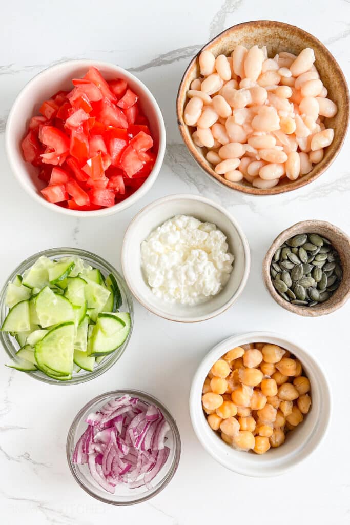 Dense Bean Salad Ingredients &ndash; Navy beans, chickpeas, sliced English cucumber, diced tomatoes, sliced onion, creamy cottage cheese, pumpkin seeds and Mediterranean dressing.
