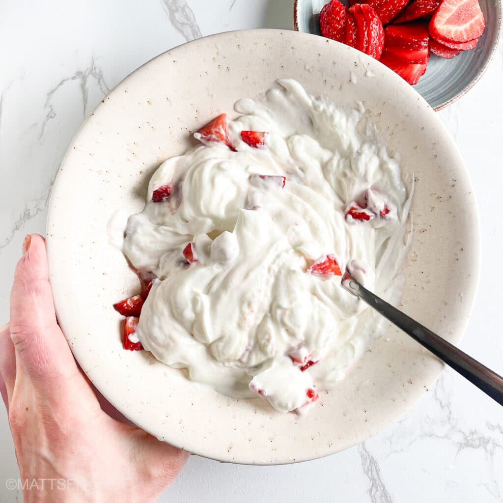 Stirring Greek yogurt and honey with diced strawberries