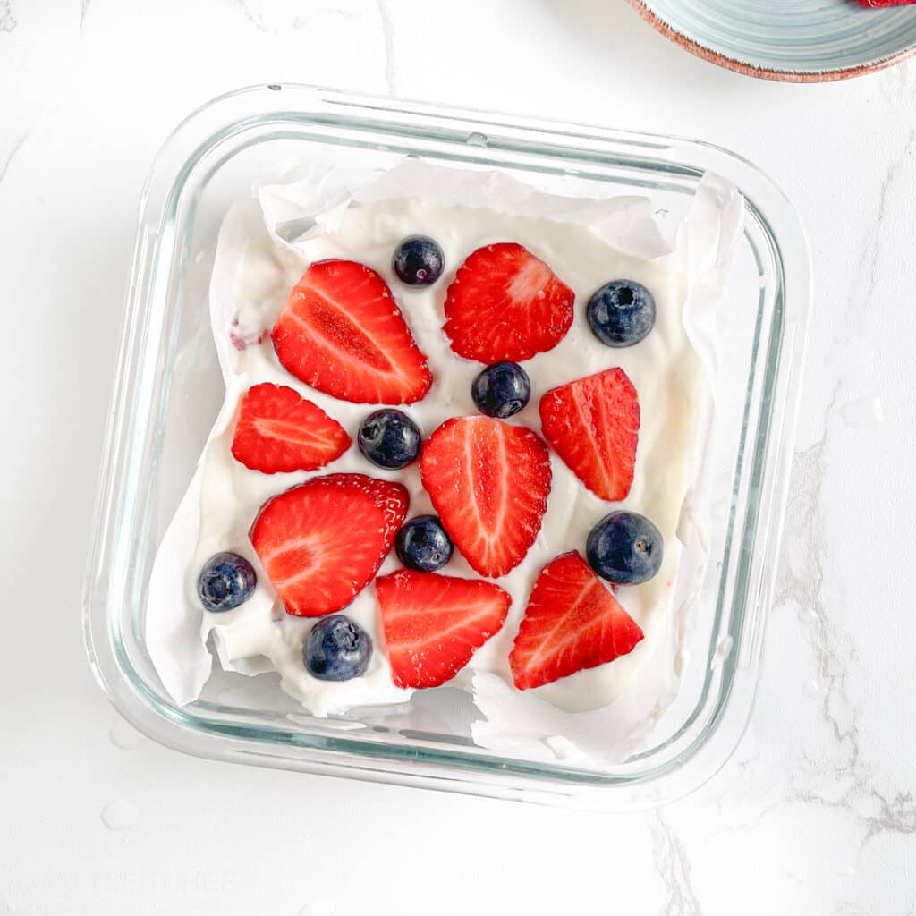 Greek yogurt bars topped with sliced strawberries and blueberries, before freezing
