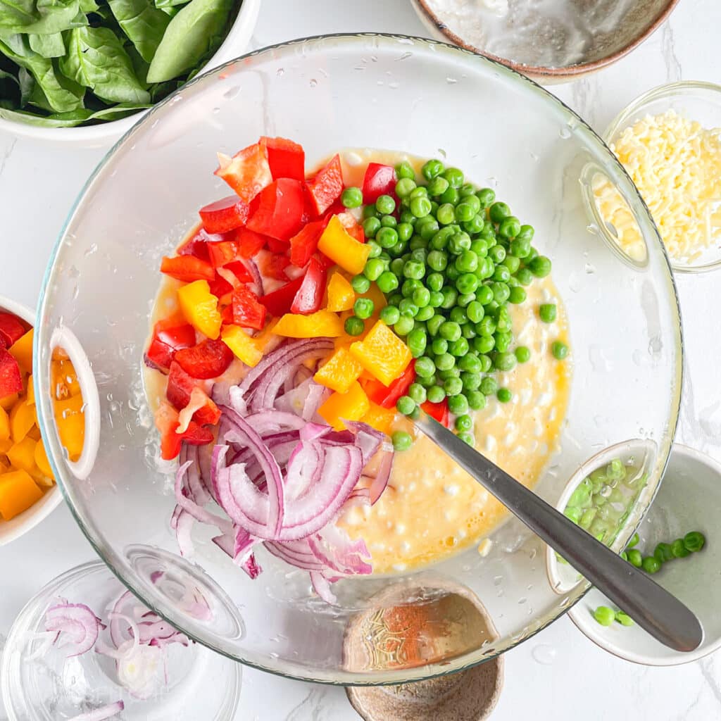 Adding diced bell peppers, sliced onion and peas to eggs
