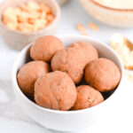 PB2 protein balls in a white bowl, with peanuts and powdered peanut butter in background