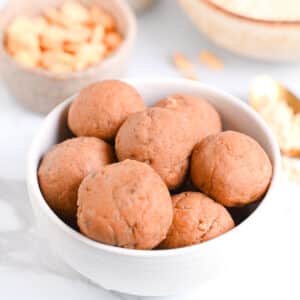PB2 protein balls in a white bowl, with peanuts and powdered peanut butter in background