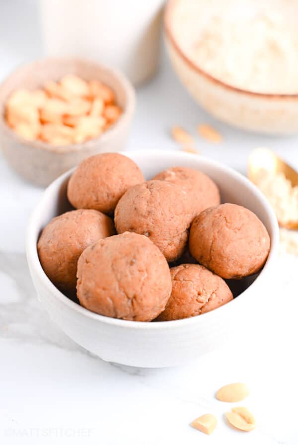 PB2 protein balls in a white bowl, with peanuts and powdered peanut butter in background