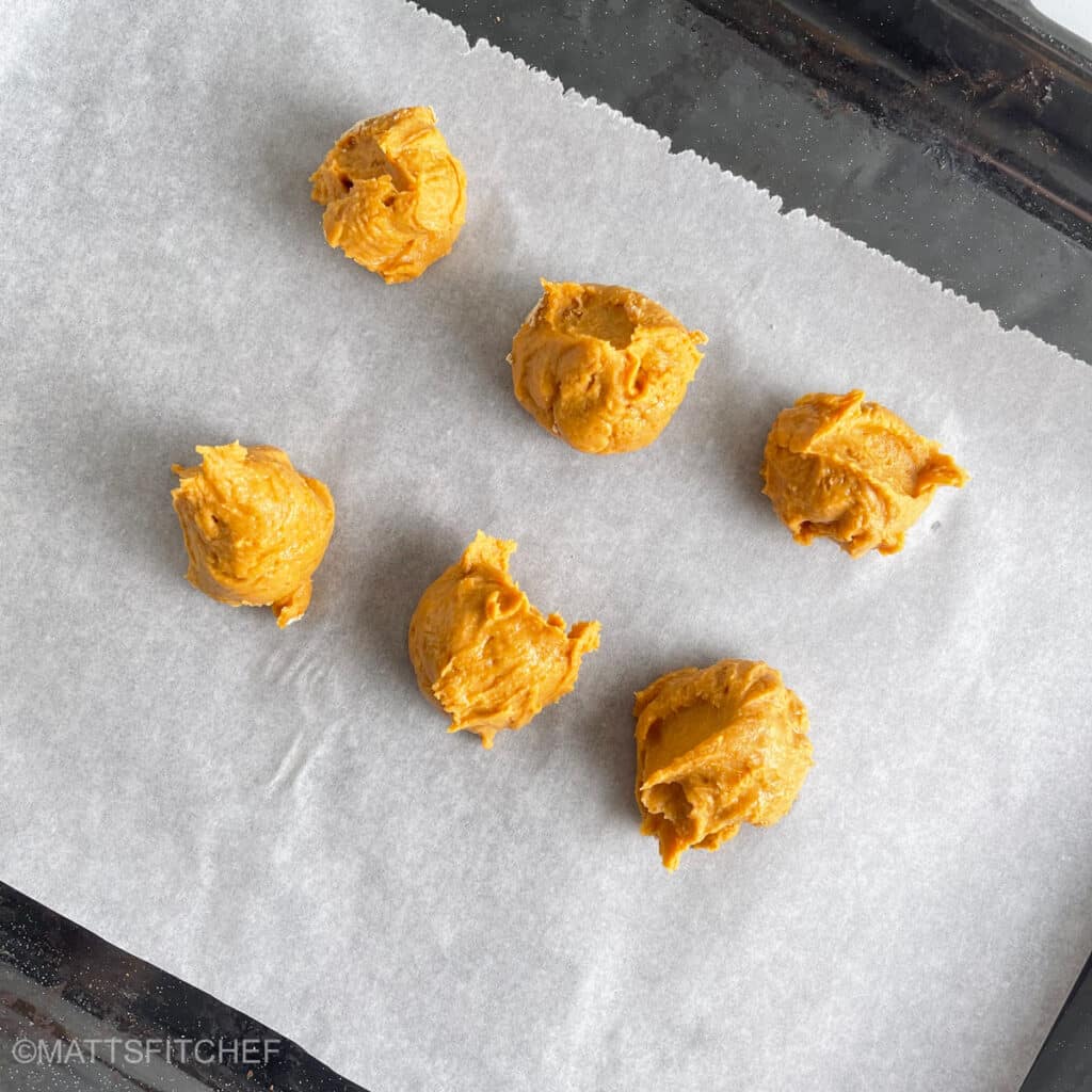 Six cookie dough balls over parchment paper lined baking sheet