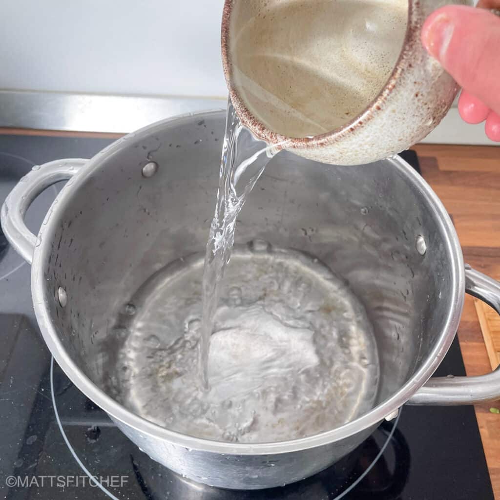 Pouring one cup of cold water in a large pot for steaming sweet potatoes
