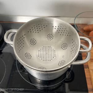 Metal strainer in large pot filled with water, ready to fit sweet potatoes for steaming