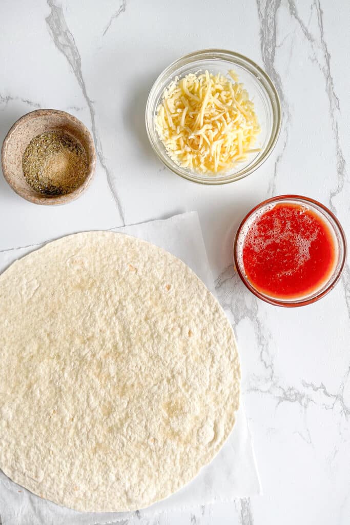 Tortilla pizza recipe ingredients &ndash; tortilla wrap, pizza sauce, shredded mozzarella cheese, optional seasonings