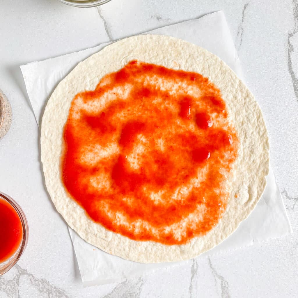 Pizza sauce spread on tortilla wrap