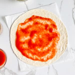 Pizza sauce spread on tortilla wrap