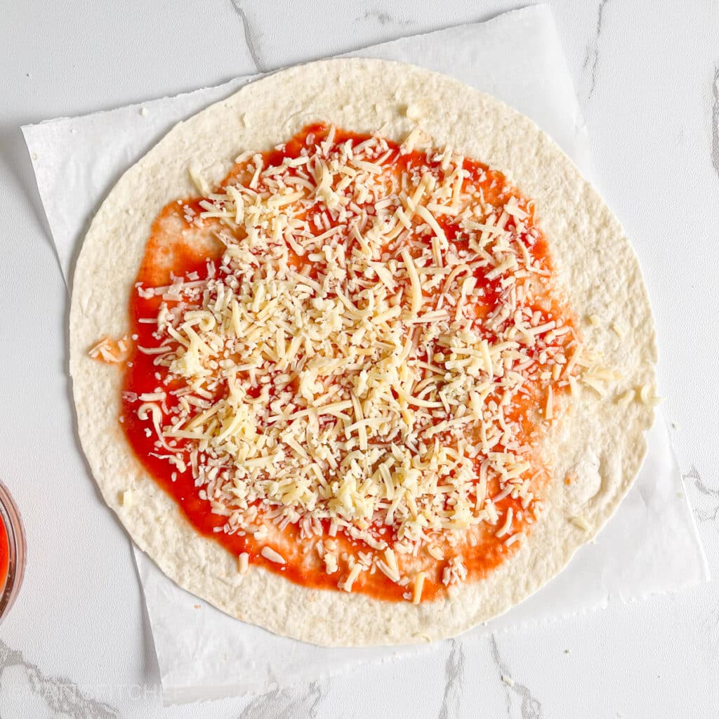 Sprinkling shredded mozzarella cheese on top of tortilla base