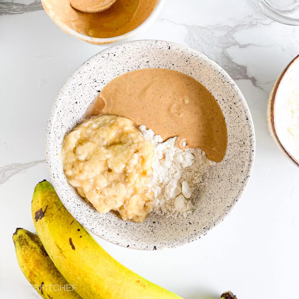 Protein powder, mashed banana and peanut butter in a bowl, ready to mix into a dough