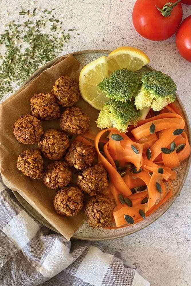 Top view of vegetarian lentil meatballs in a serving plate with carrot spaghetti, broccoli and lemon slices